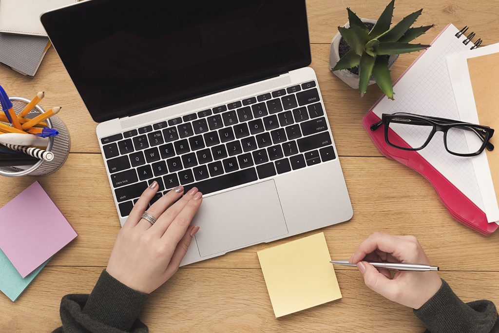 Woman typing on laptop computer and writing notes